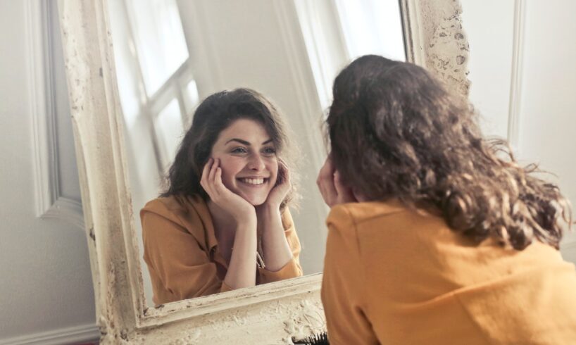 Kvinde smiler og kigger i spejl på sig selv